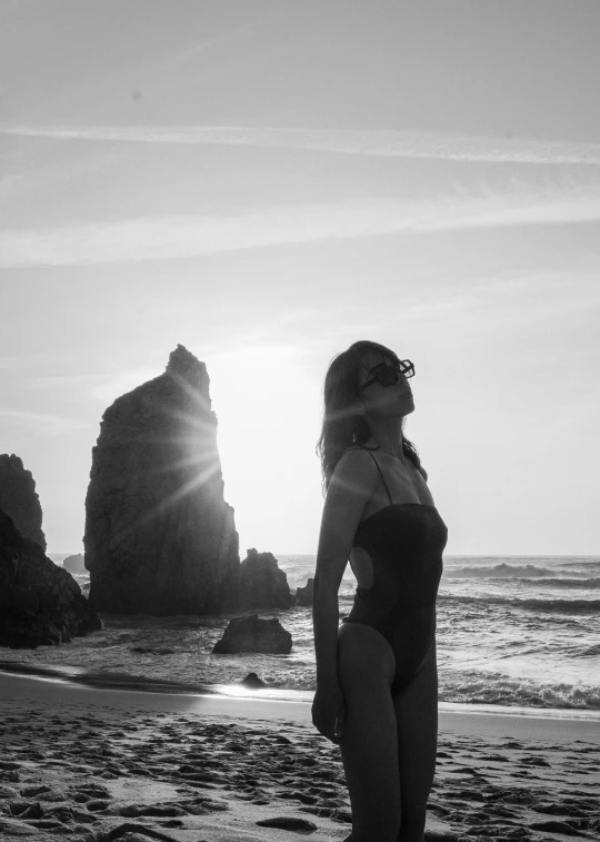 a woman standing on a beach in a bathing suit looking out into the ocean