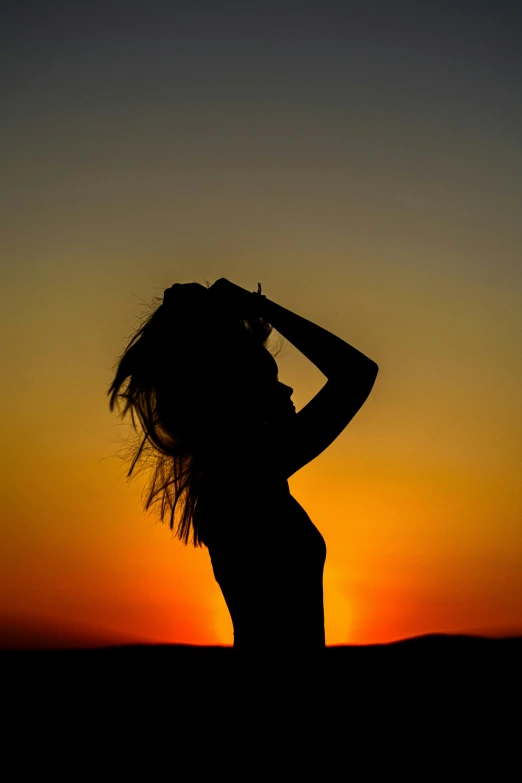 a woman standing in front of a sunset with her hands on her head