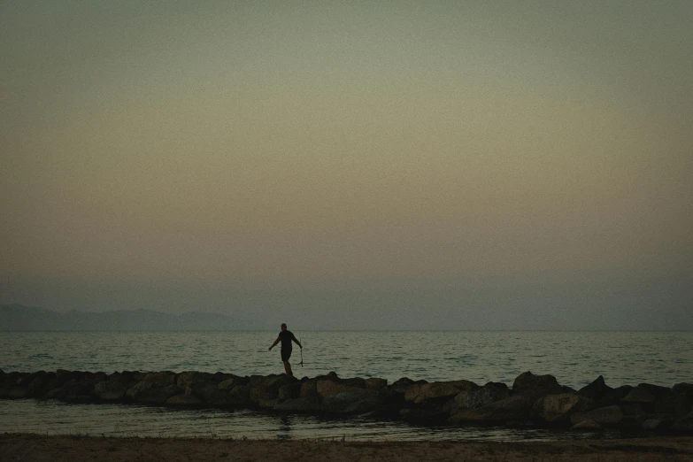 silhouette of person standing on rock looking over water and clouds