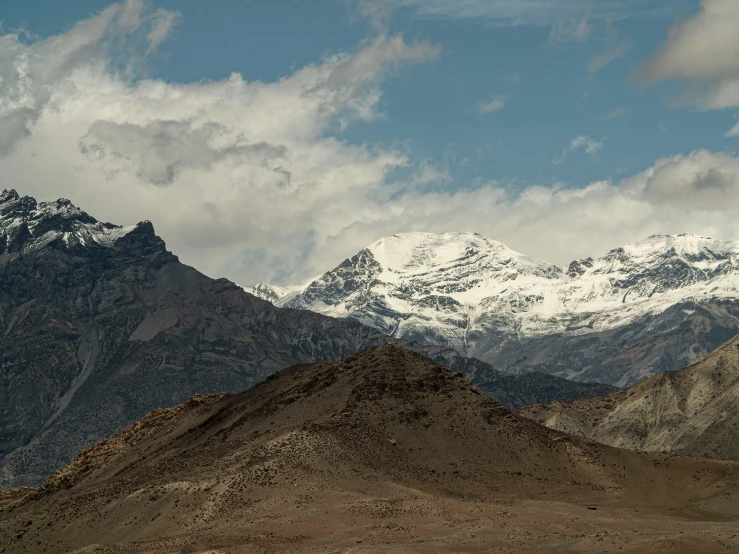 a mountain range with snow on top, and some clouds