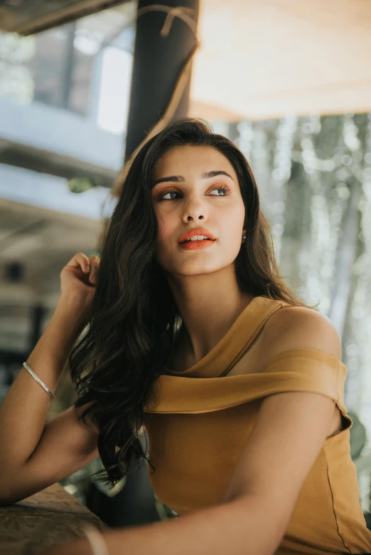 a young woman in a brown shirt leaning against a wooden table