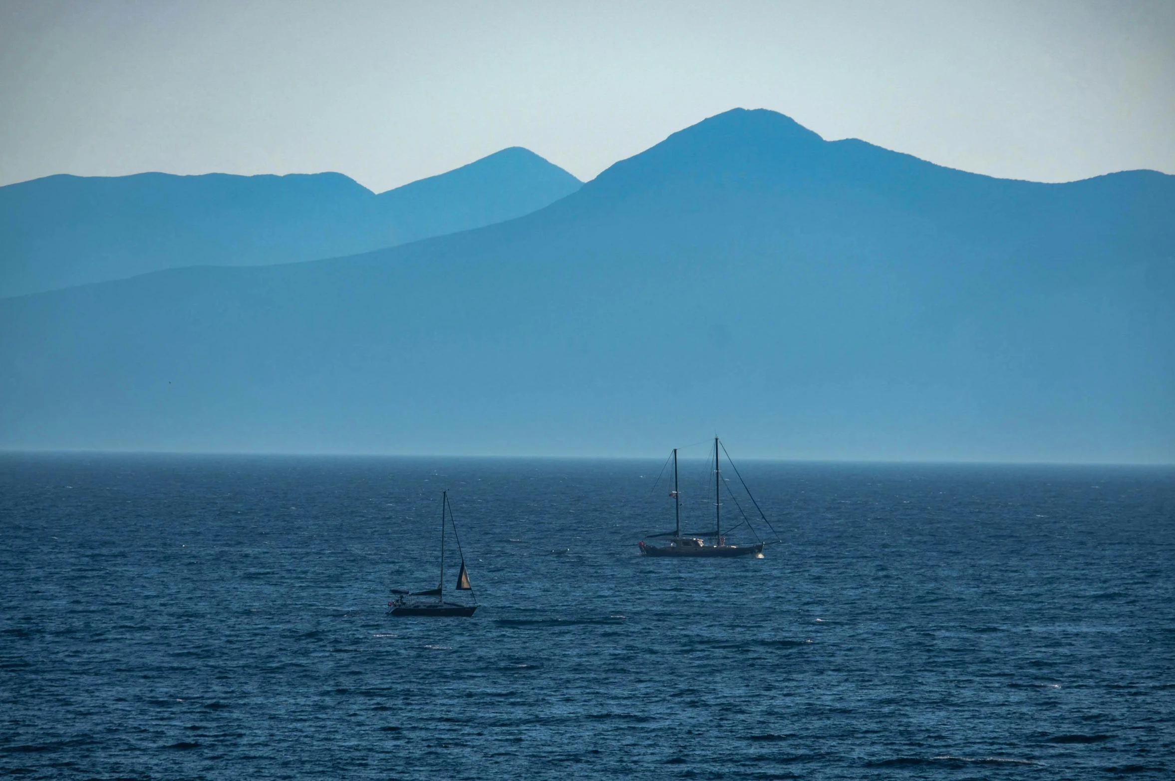 two boats floating on top of the ocean with mountains in the distance