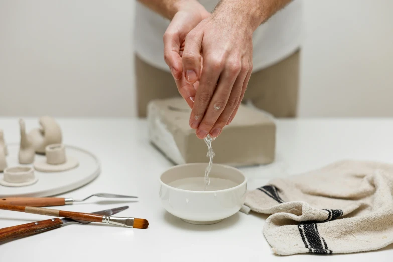 person putting water into bowl with pottery tools
