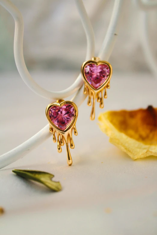 a pair of pink earrings hanging from white strings