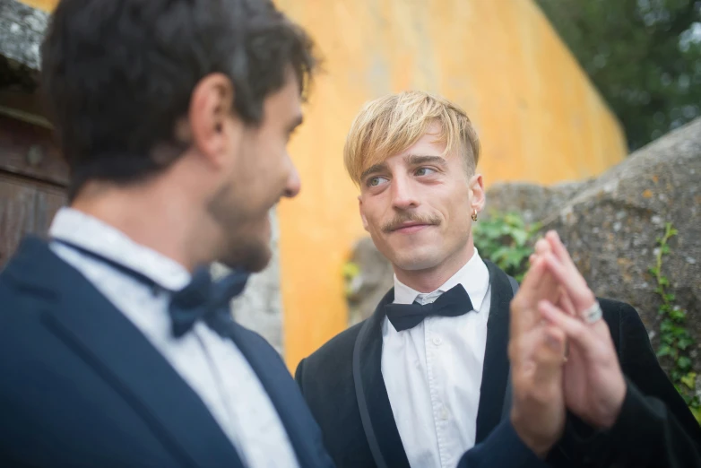 two men are standing outside in suits and bow ties