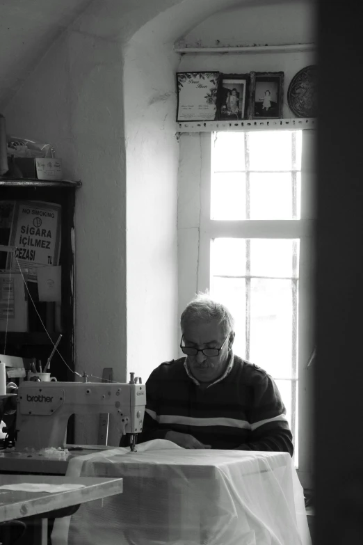 a man in glasses sits in front of an sewing machine