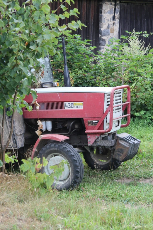 the small tractor is parked in the grass near a wall