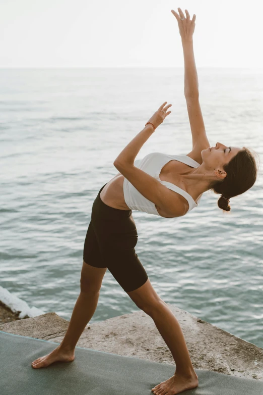 a young woman is doing a yoga move by the water