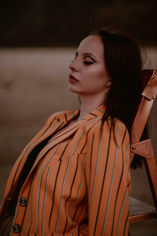 a girl is seated wearing an orange jacket and earrings