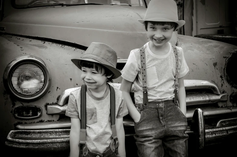 two boys are standing in front of an old car