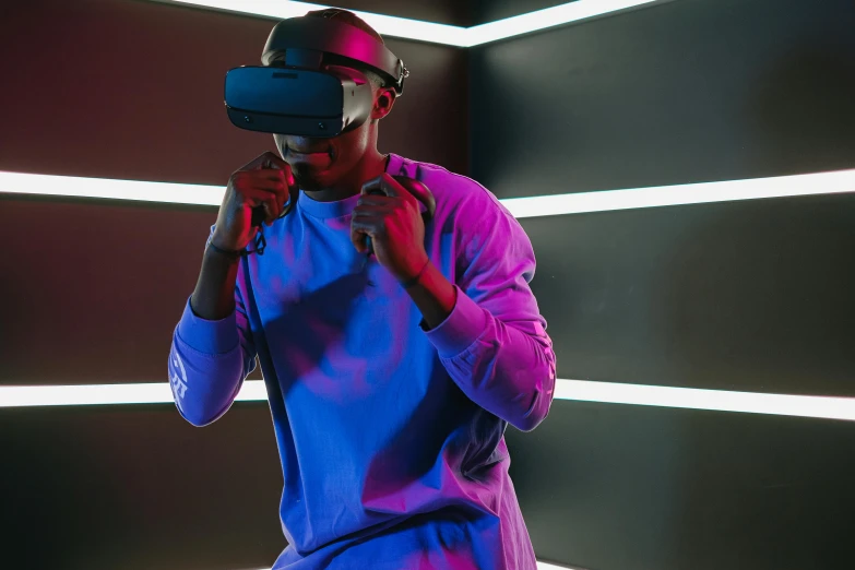 a man wearing a blue shirt and a pink jacket looks into a virtual reality headset in front of a green wall with stripes