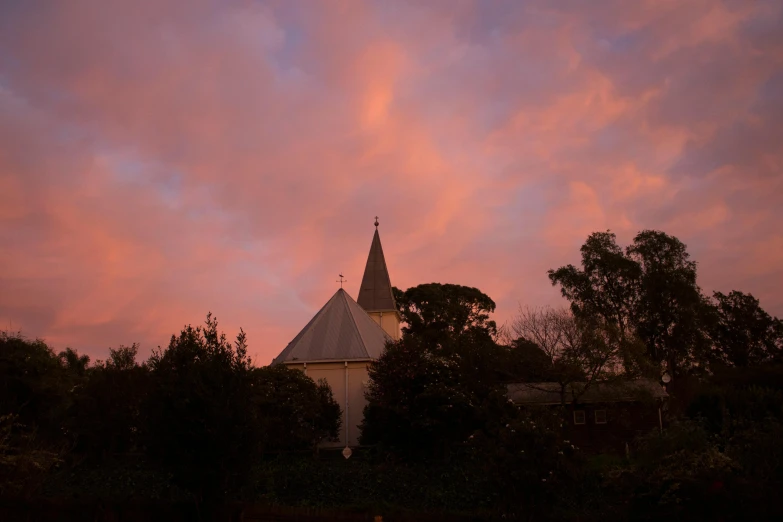 a sunset with some clouds and trees and some buildings