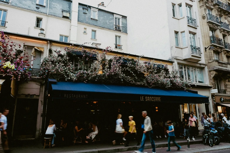 people walk past shops decorated with flowers