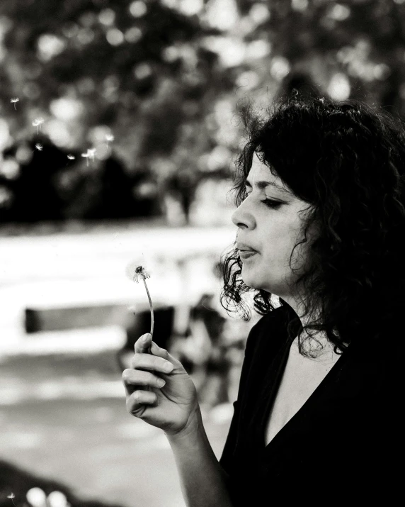 woman blowing a dandelion with her hair in the wind