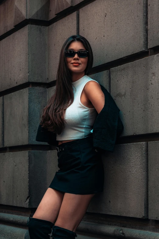 a woman posing for the camera while standing against a stone wall