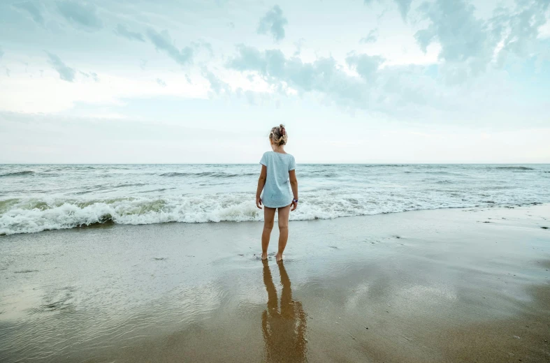 a woman standing on the beach looking out at the water