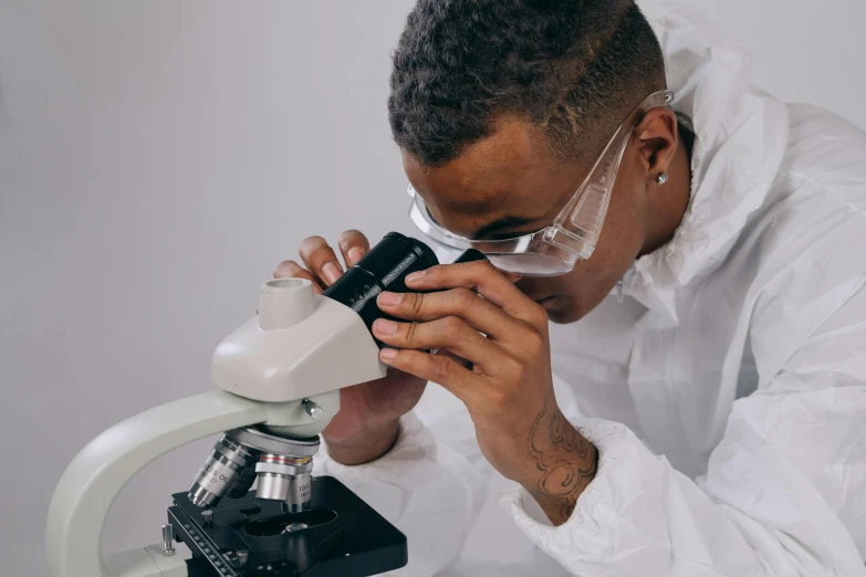 a young male in a white lab coat looking at soing under a microscope