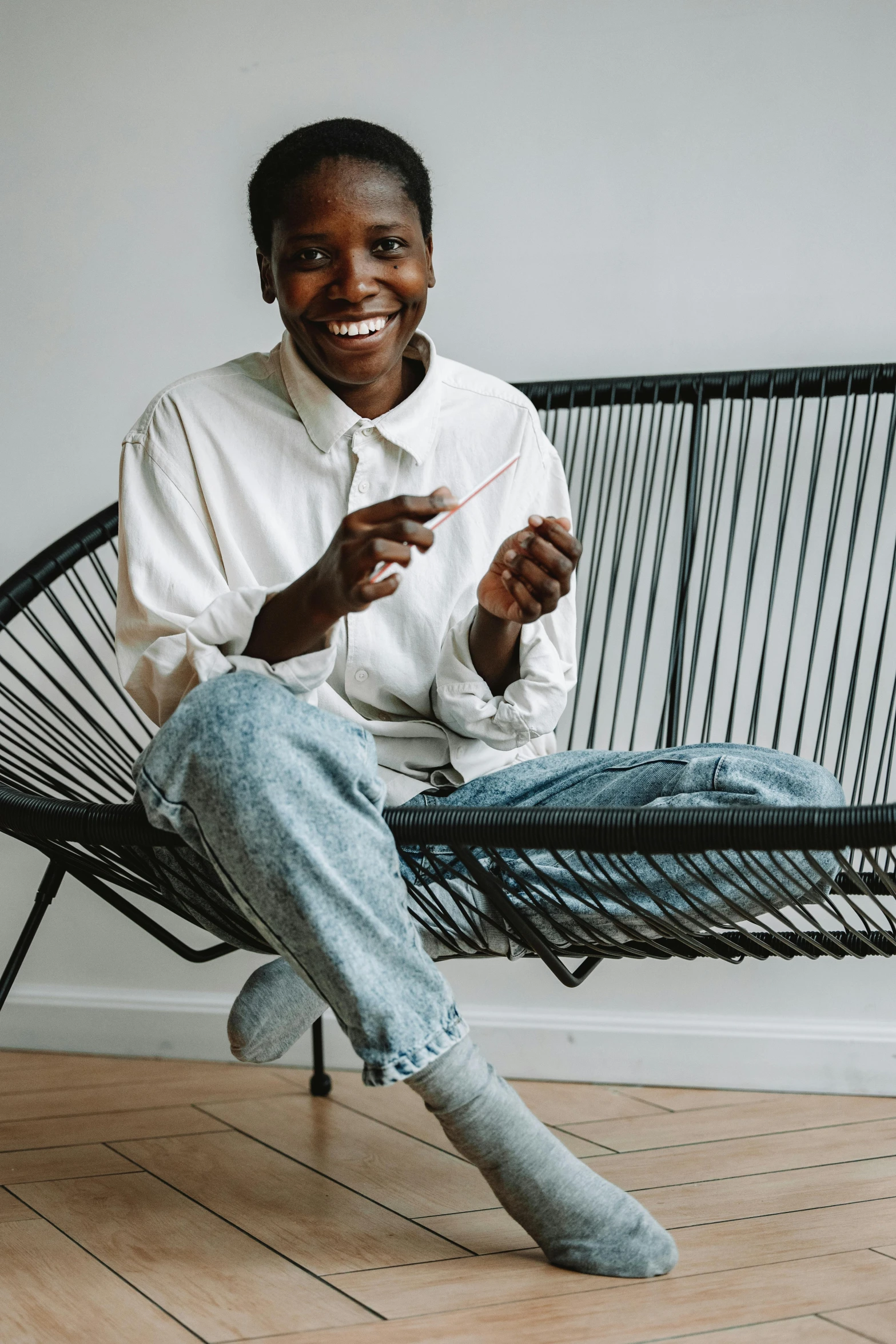 a smiling man wearing an unoned white shirt and blue jeans sits on a bench