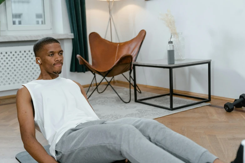 a man in a white tank top reclines on a grey mat