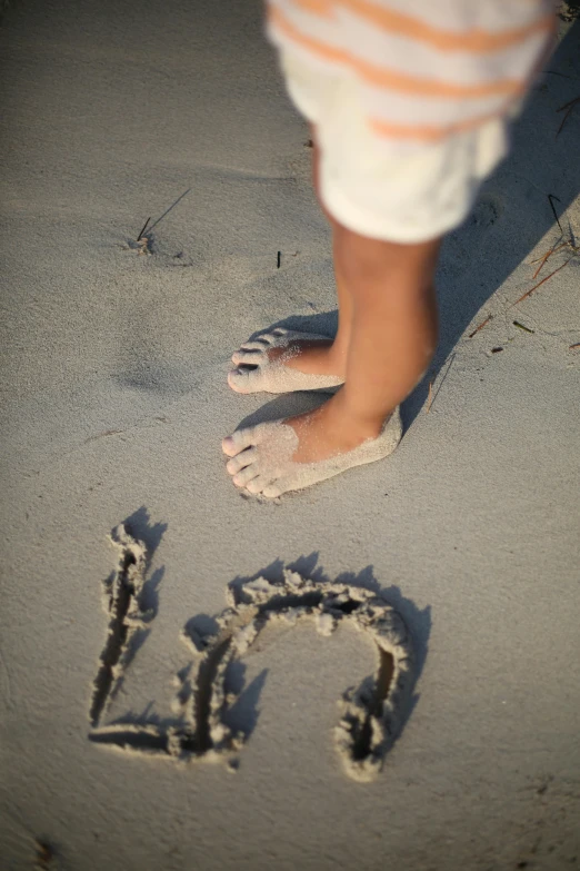 a small child's feet and writing in the sand