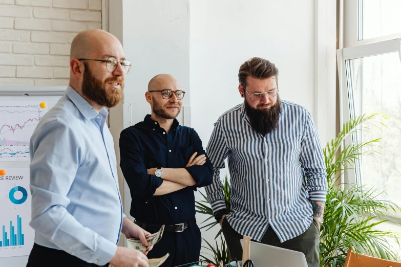 a couple of men standing around a table looking at a laptop computer