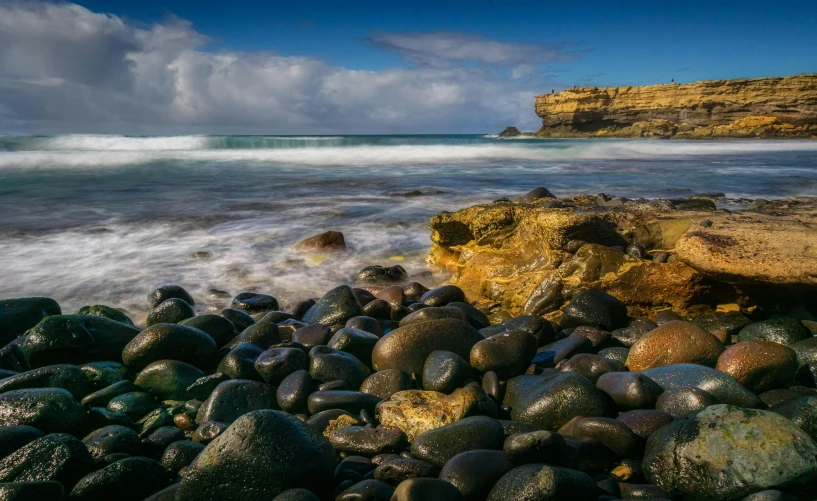 a wave rolls in behind a beach with rocks