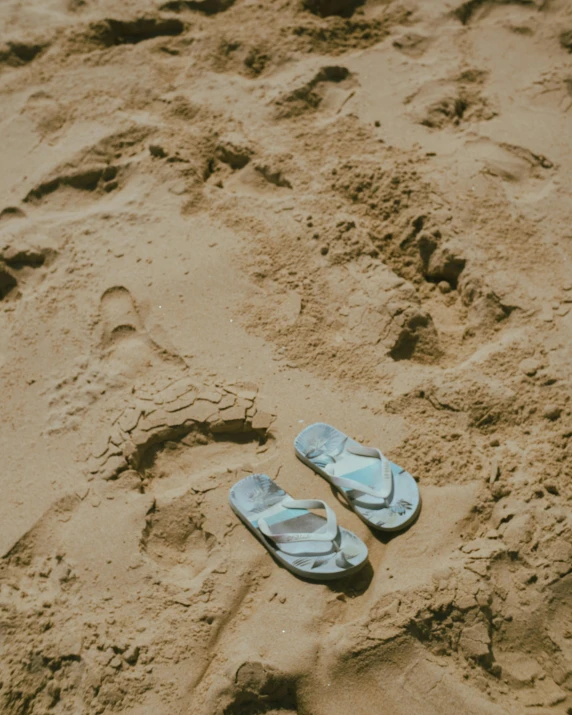 two pairs of sandals on the beach with a wave coming in