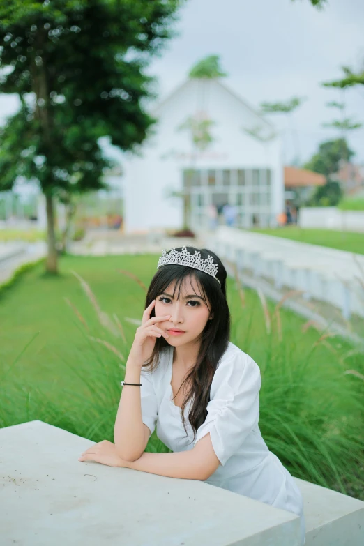 the woman sits on a stone bench with grass and bushes in front of her