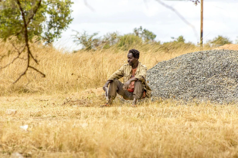 a man in a field sitting down next to a huge stone