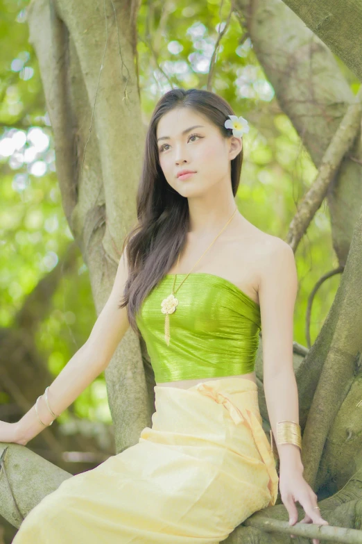 a beautiful woman sitting in a tree wearing a yellow dress