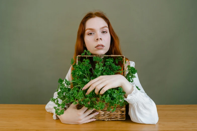 a woman sitting in front of a wooden table while holding onto a basket of green vegetables