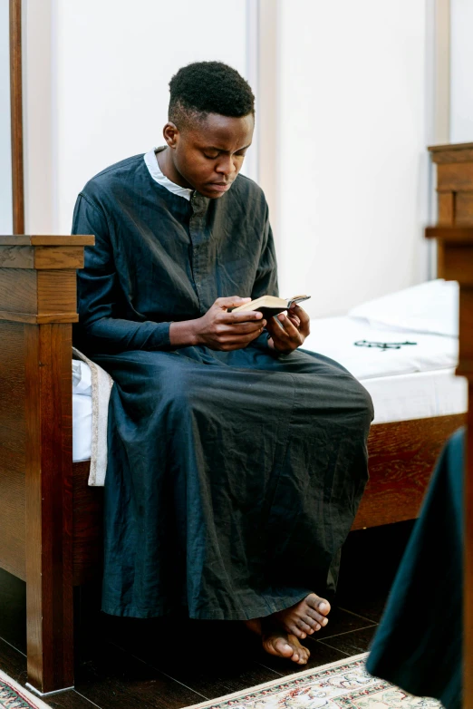 man in black outfit looking at his phone while seated on a bed