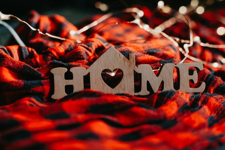 wooden home sign on bed with christmas lights around it