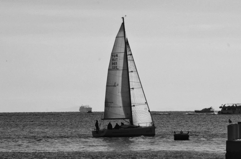 a sailboat floating in the ocean with a ship behind it