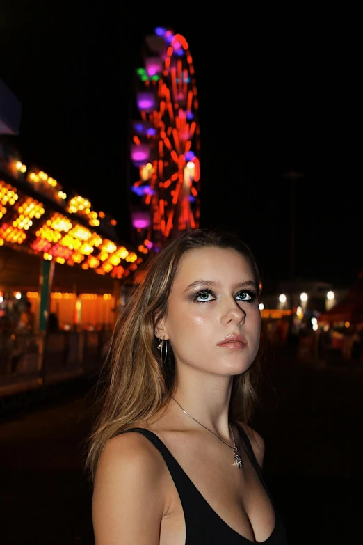 a beautiful young lady with large booches standing next to a ferris wheel