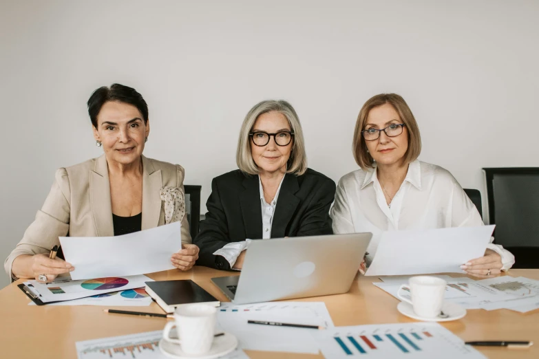 three women sitting at a table with papers and laptop