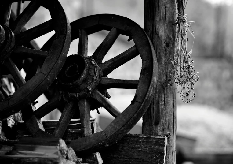 an old wooden cart wheel sits by the barn wall