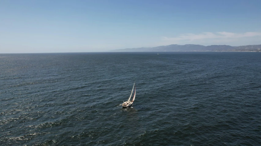 sailboat in large ocean next to rocky shoreline