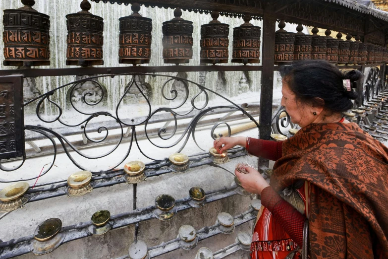 an indian woman wearing an ethnic costume looks through a fence at gold hanging objects