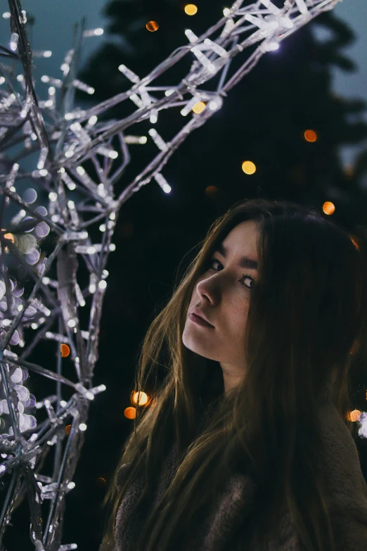 a woman standing next to some trees with lights all over it