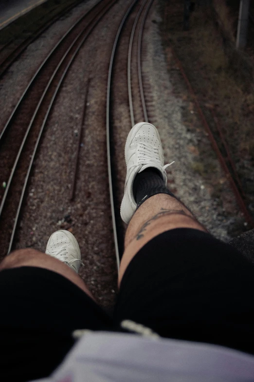 person sitting on train tracks wearing white shoes