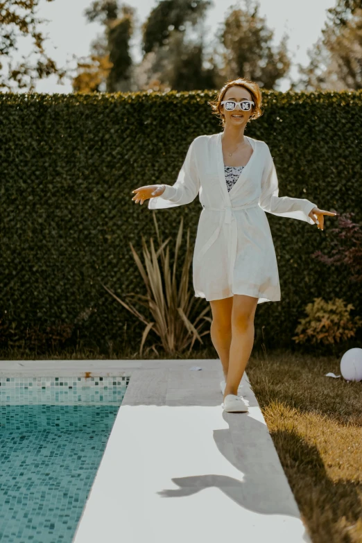 a woman in white clothing standing on a platform by a pool