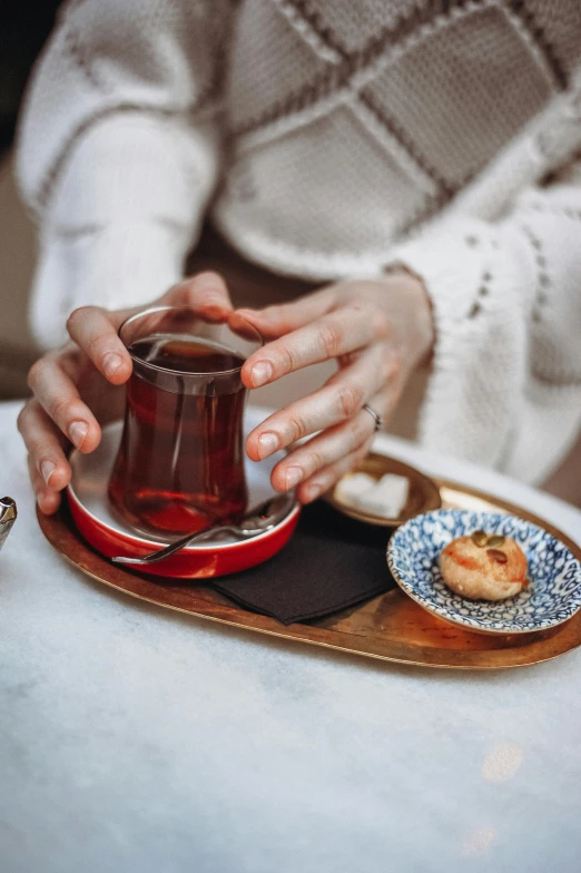 a person with their hands in a glass on a tray and another hand holding a pastry