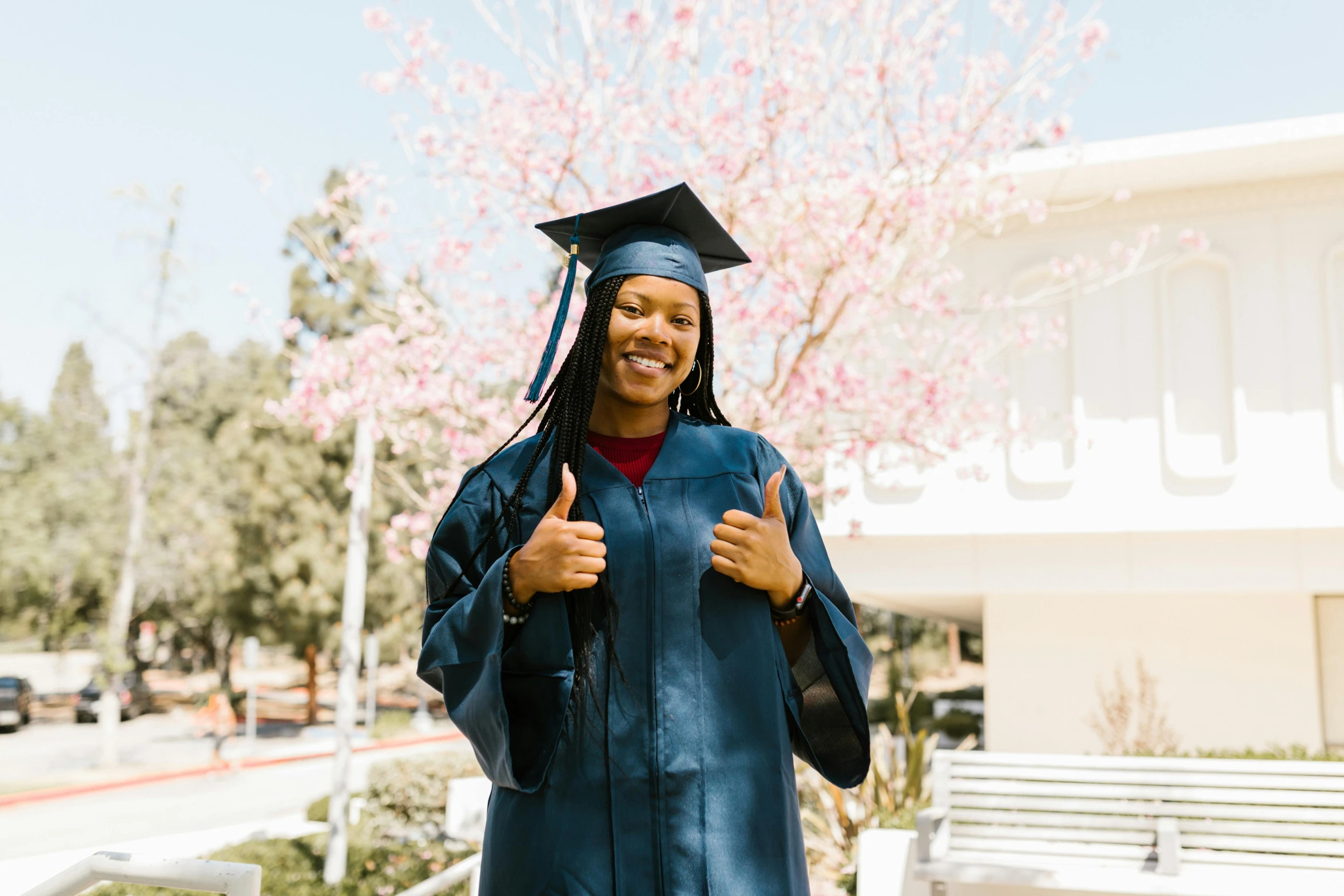 the woman wearing a graduation hat and gown holds her thumbs up
