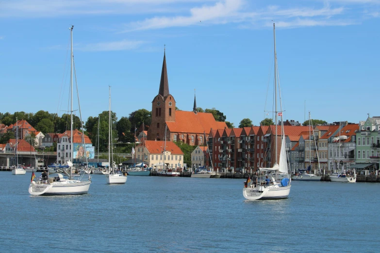 several sailboats on the water in front of a building with a spire