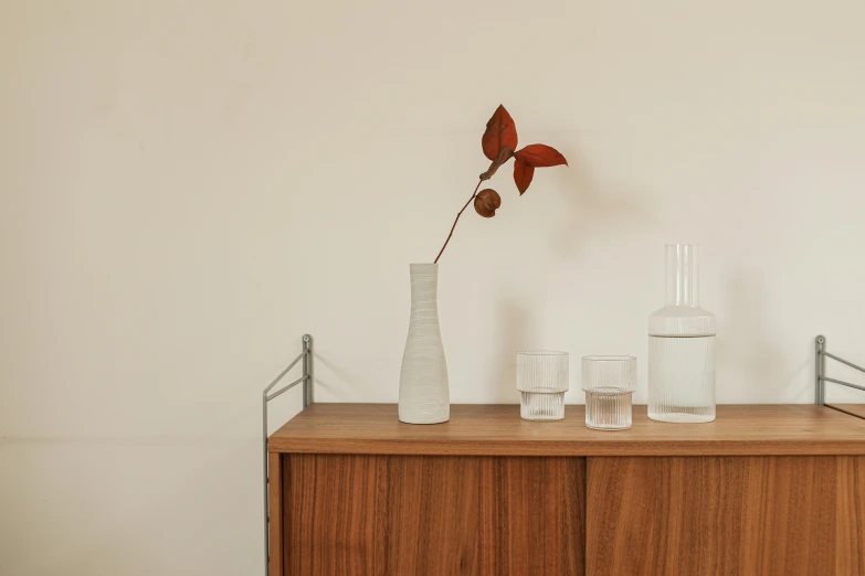 the large white vase has a single stem, several glasses and a vase with an orange flower