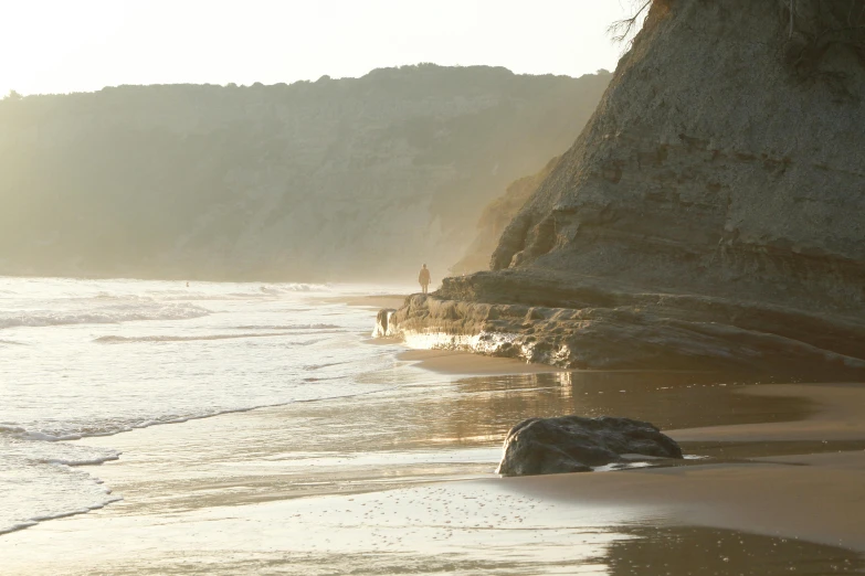 a man standing on the beach next to a rock