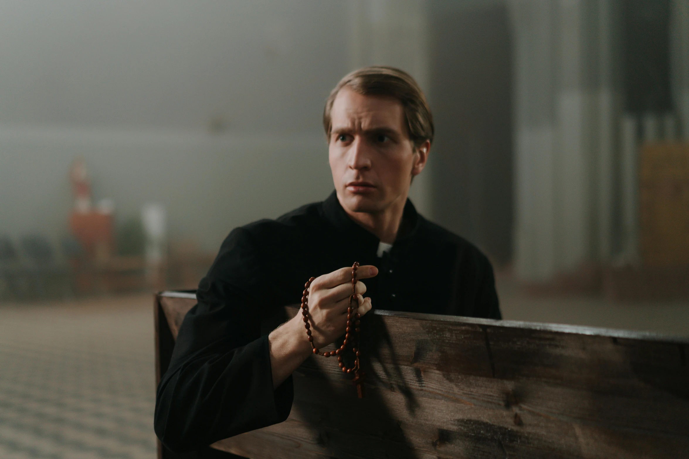 man holding rosary by hand standing next to wooden wall