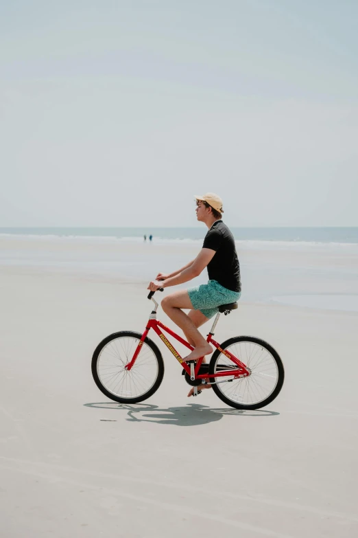 a man riding a red bike across a sandy beach