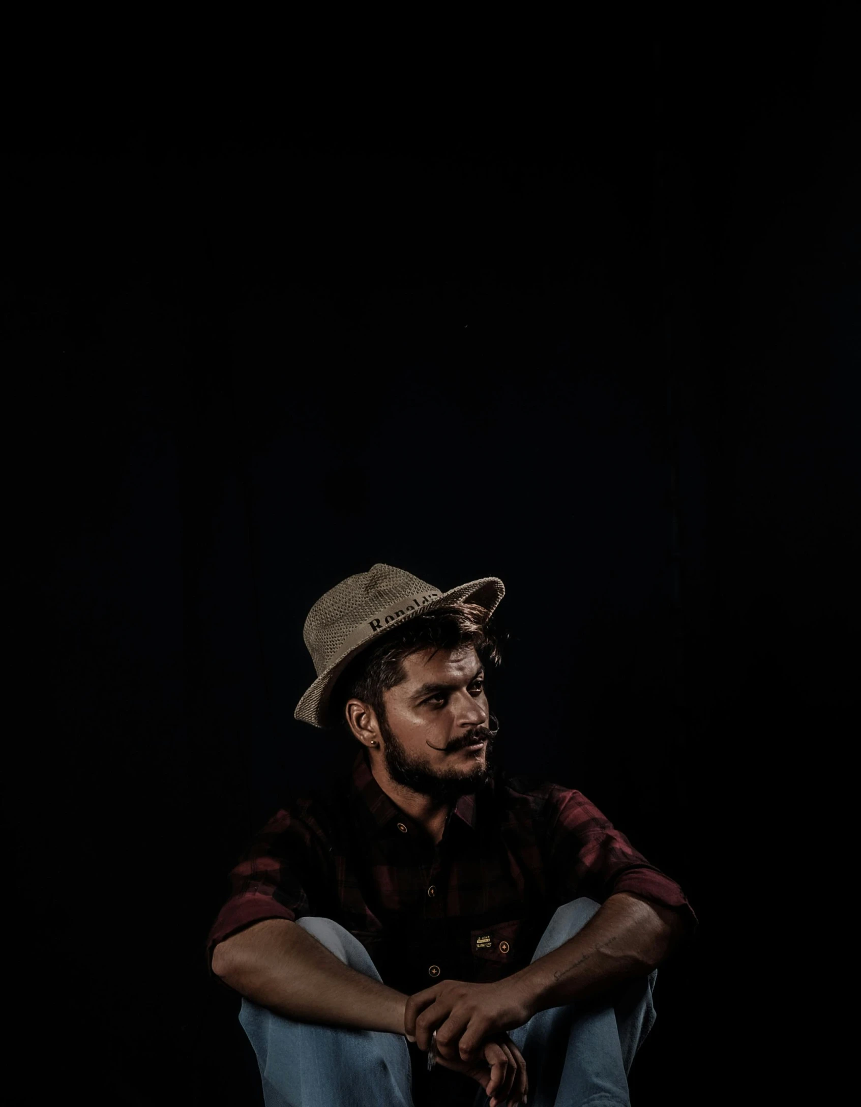 a man in a hat sits in the dark, his hands behind him